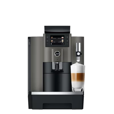 Un JURA W8 Dark Inox (SA) avec un affichage numérique, un corps argenté et noir et un mousseur à lait attaché. Un verre rempli de lait et de café en couches est placé sous le distributeur de lait.