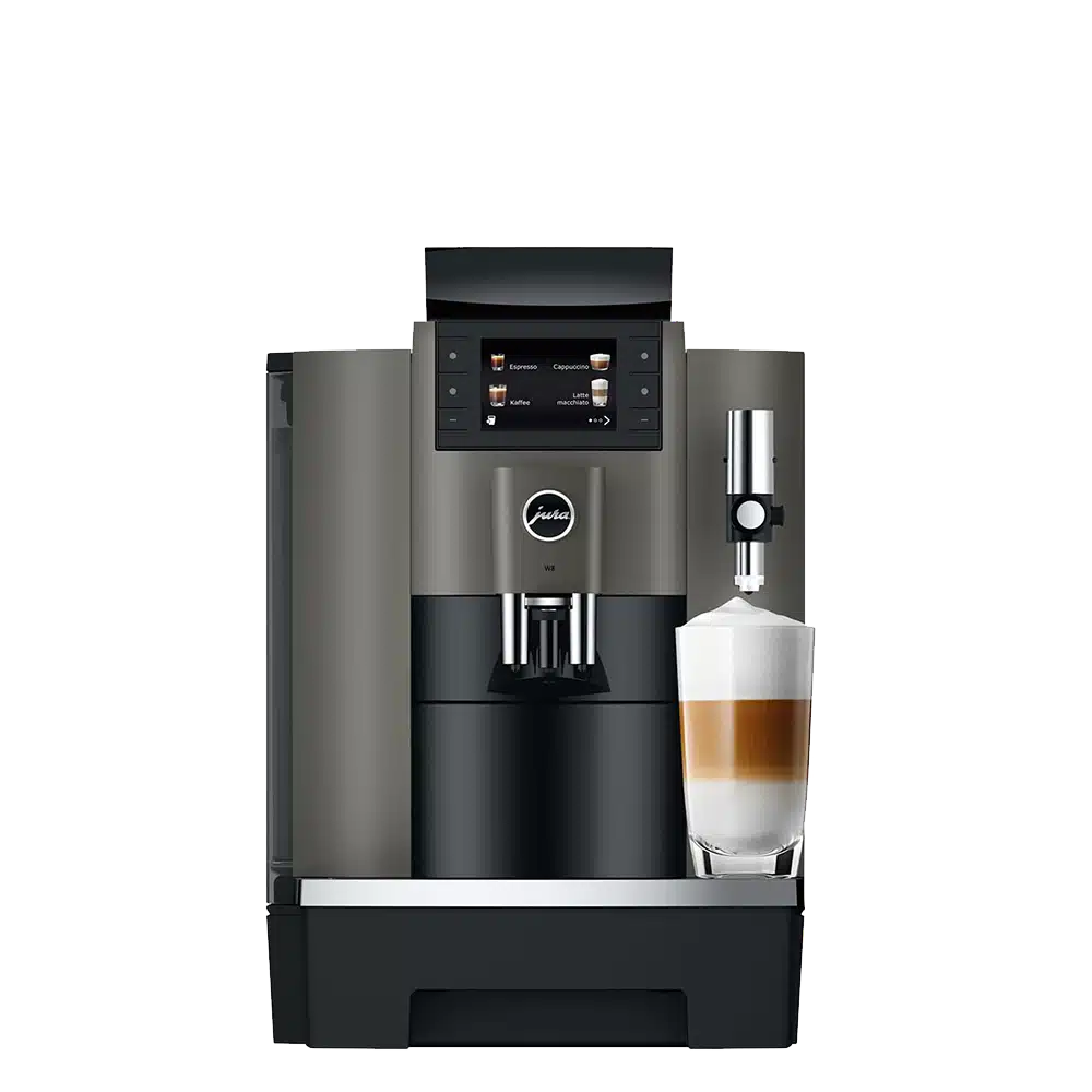 Un JURA W8 Dark Inox (SA) avec un affichage numérique, un corps argenté et noir et un mousseur à lait attaché. Un verre rempli de lait et de café en couches est placé sous le distributeur de lait.