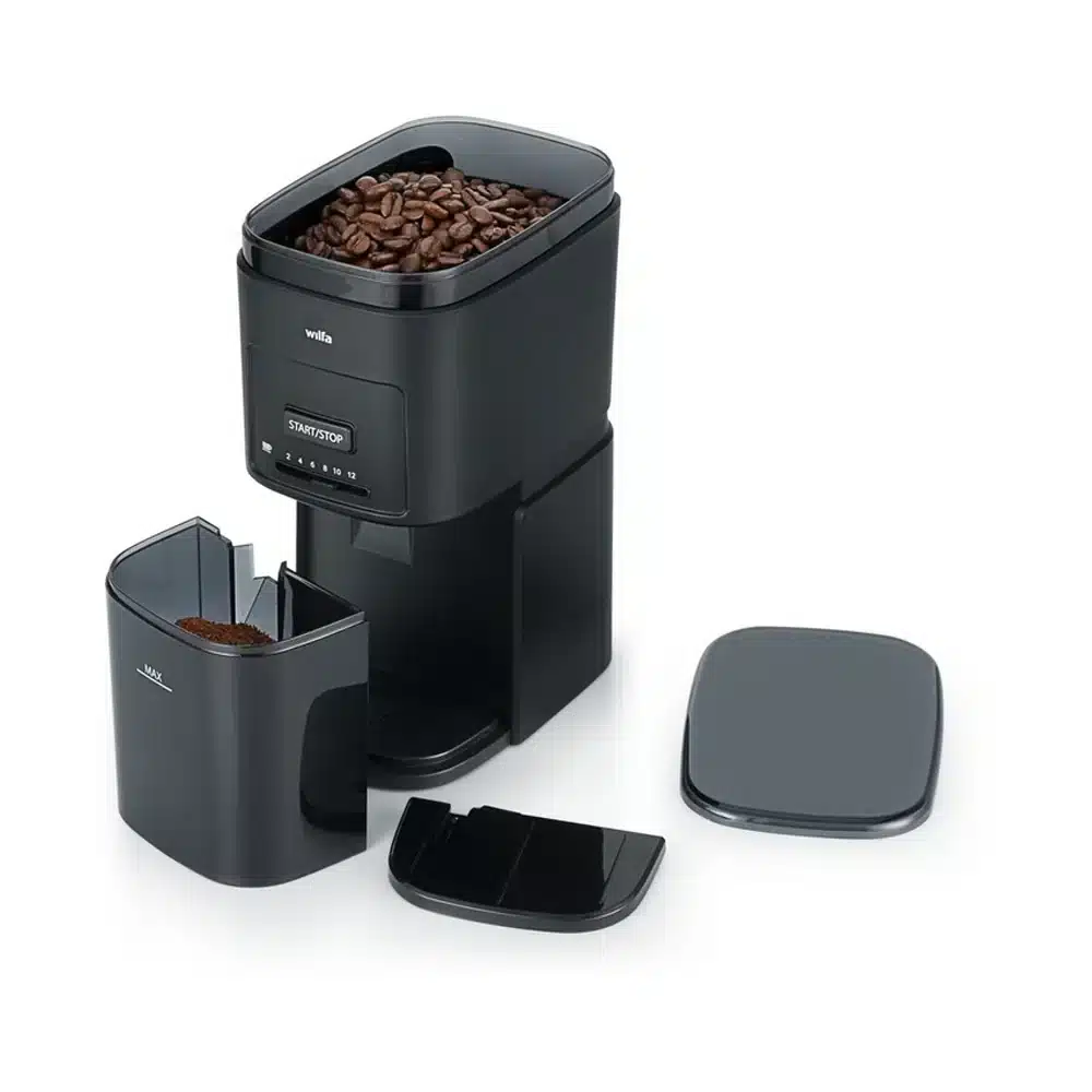 Die Wilfa Kaffeemühle Il SOLITO (Copie) ist eine schwarze Kaffeemühle mit offenem Deckel, die mit Kaffeebohnen gefüllt ist. Unterhalb der Mühle befindet sich ein separater Behälter für gemahlenen Kaffee. Um die Mühle herum sind verschiedene abnehmbare Teile angebracht, darunter ein Deckel und eine Schaufel.