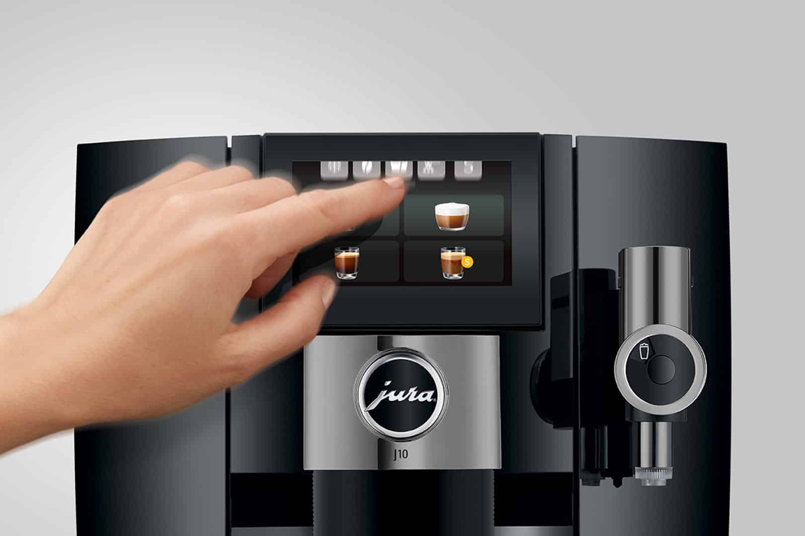 Une main sélectionne une option de café sur l'écran tactile d'une machine à café Jura J10. L'écran affiche différentes icônes de café telles que l'espresso, le cappuccino et le latte, avec le design noir et argent élégant de la machine également visible.